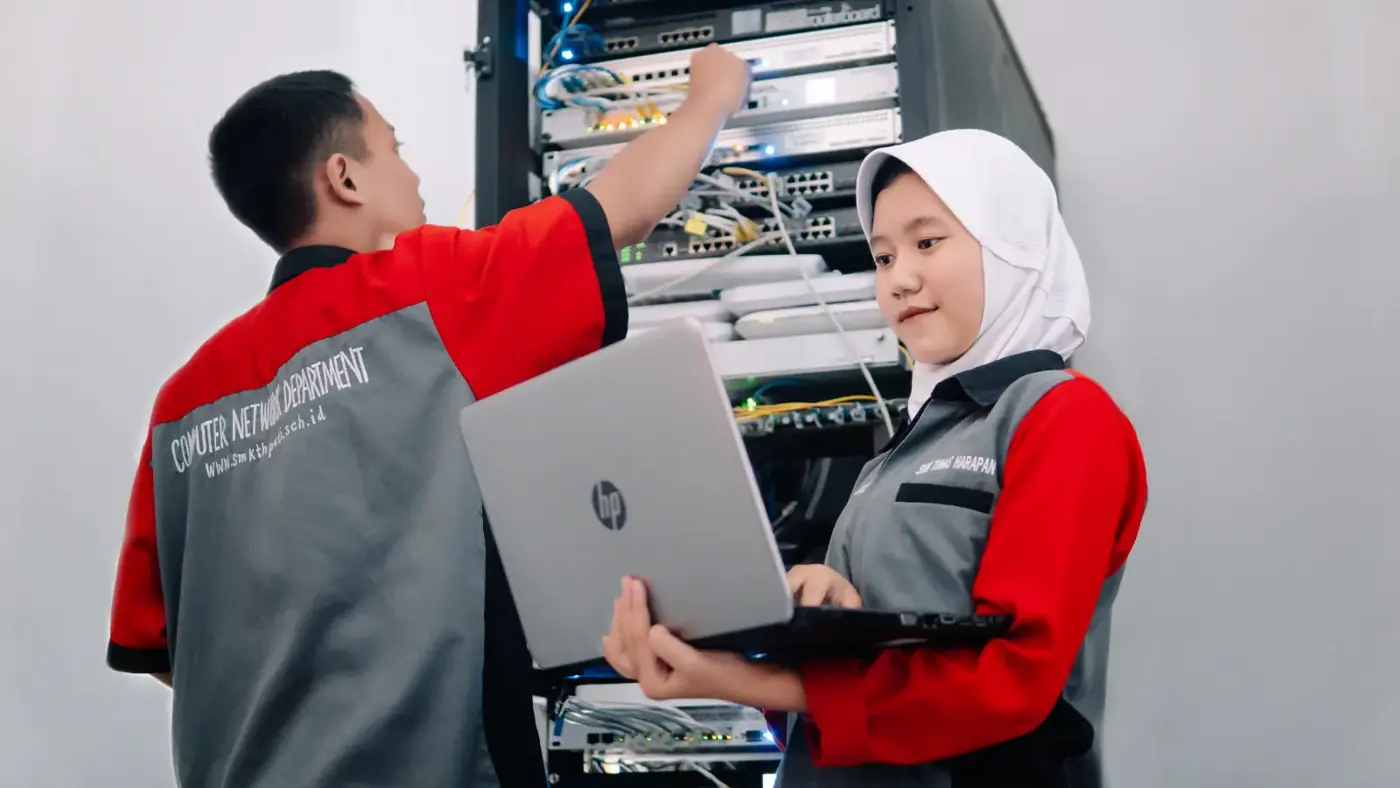 Siswa mengatur kabel dan perangkat di rak jaringan